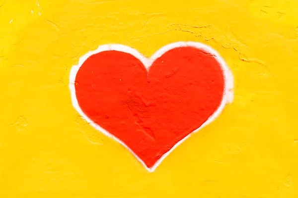 Ein leuchtend rotes Herz, das auf eine gelbe Wand gemalt wurde. Fotografiert von Nicola Fioravanti über unsplash.com