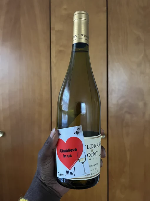 Wine bottle with white wine and a sticker cover the labeling with To: You, “I chablieve in us” in a big red heart , From: Me!, a wine glass and a dog.