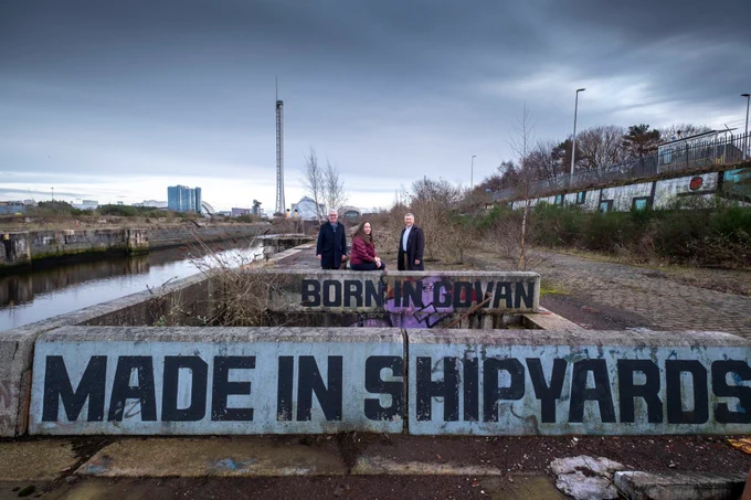 A photo of three people standing at Govan shipyards. From left to right is Des McNulty, Honorary Fellow, Civic Partnership and Place Leadership, at the University of Glasgow, Professor Jaime Toney, director of the University of Glasgow’s Centre for Sustainable Solutions, Duncan Booker, COP26 Stakeholder Manager at Glasgow City Council. In front of them are signs that say, Born in Govan, made in shipyards.