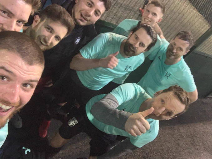 8 men in mint green tee shirts give a thumbs up to the camera as they take a celebratory selfie