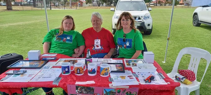 Melissa with two others sitting at a market stall table selling her clothes. 