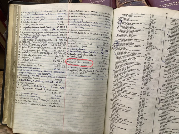 An open book with left page handwritten and the opposite page printed. It lists subjects and their library class marks.