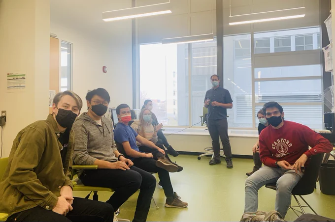 Photo of students wearing masks looking at the camera with a professor standing at the front of the room