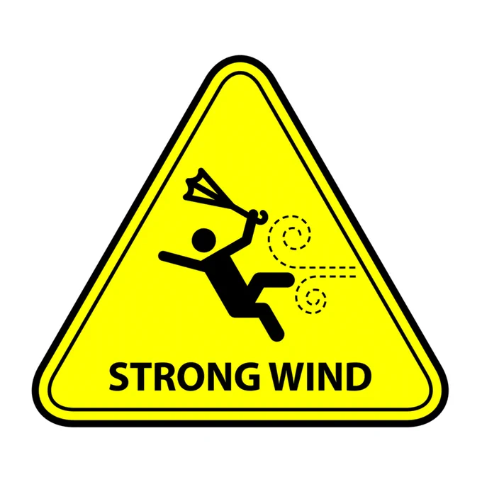 A triangle warning sign with a figure in the centre blown backwards by high winds, and an umbrella turned inside out. Underneath are the words 'Strong wind'.