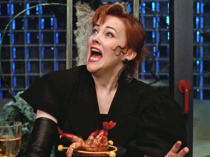 Catherine O'Hara in Beetlejuice. She is singing at a dinner table,