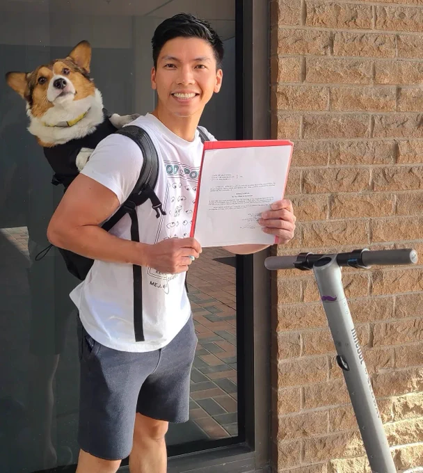 Picture of Kenneth holding Kirby the corgi in a backpack and him holding his certification from the City Clerk's office stating he qualified to get on the ballot