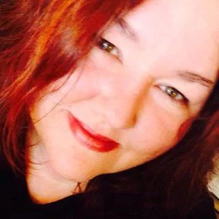 A cropped, close-up photo of  June Knightly, a white woman with red hair. She is smiling at the camera. 