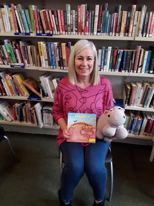 Local author holds her book in front of library shelves