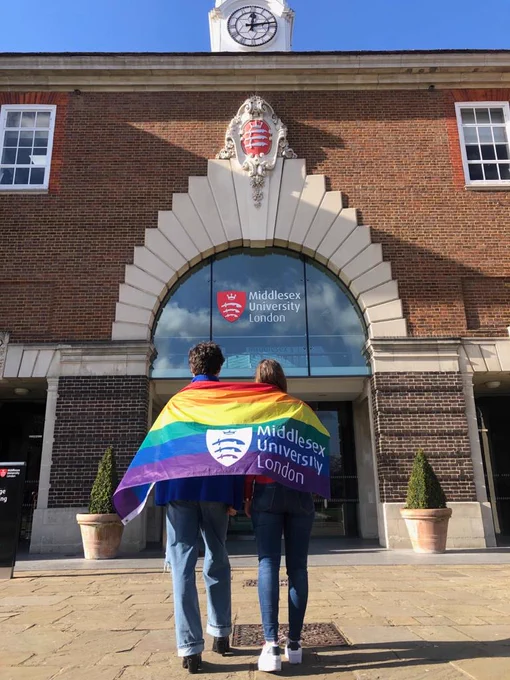 Two students walking into College Building on campus, with a rainbow flag wrapped around them both