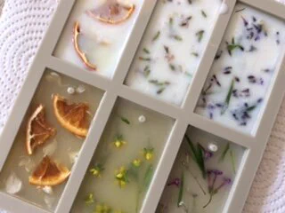 Rectangular shaped wax mould tray filled with wax. Each compartment has a different natural ingredient in - including dried lemon, dried oranges, lavender and buttercups.
