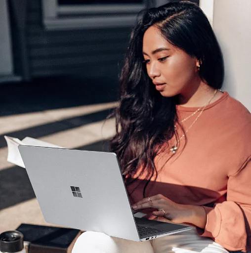 a woman sitting in the sun looking down at her laptop