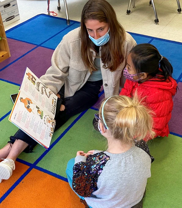 A Duke student-athlete reads a book with two elementary school students.
