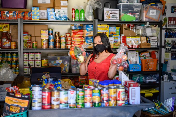 A person wearing a face mask holding up bags of fruits and vegetables