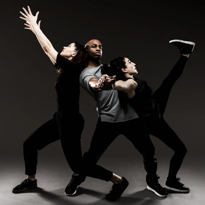 A moment from Ephrat Asherie's Odeon: Dancer Manon Bal with arms outstretched leans on Matthew West whose hand is clasped with Ephrat Asherie as she leans back on him while kicking her leg. Photo by Matthew Murphy.