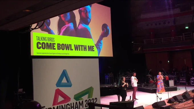 3 ppl on stage, large projected image behind reads Talking Birds Come Bowl With Me