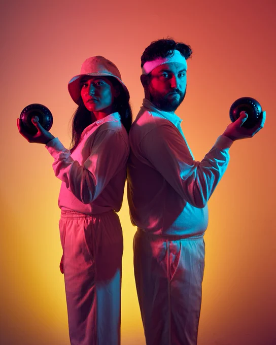Woman & man in sports gear stand back to back looking to camera, each holding a Bowl