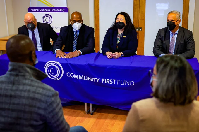 Administrator Guzman sits at a table with two other people. Sign in front of the table reads Community First Fund. All are wearing masks.