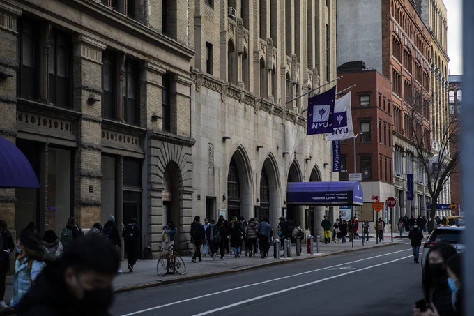 people walking on West Fourth street in shadow wtih NYU flags overhead