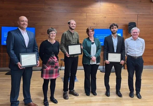 Staff and students stand in a row and smile at the camera, at the ESE Postgraduate Prizes event. Winning students hold their framed certificates.
