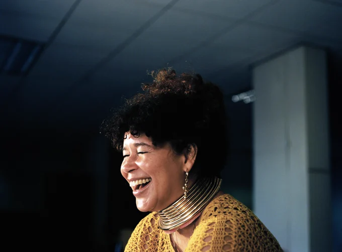 Artist Alberta Whittle laughing in a photo captured by photographer Matthew A Williams. Alberta wears a yellow dress and statement silver jewellery.
