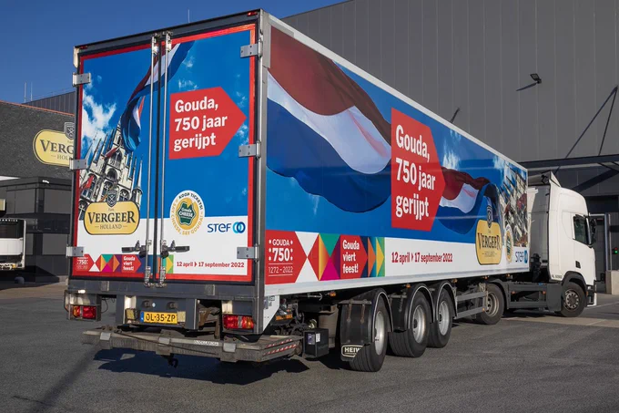 Vrachtwagen met Gouda750 logo en daarboven grote wapperende NL vlag  en de slogan ‘Gouda, 750 jaar gerijpt’