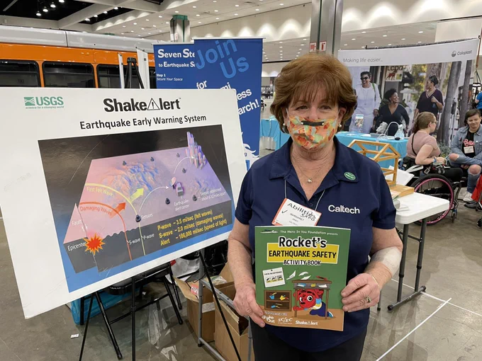 ShakeAlert team member holding copy of Rocket’s Earthquake Safety Activity Book. Behind her is a image of how the ShakeAlert system works.