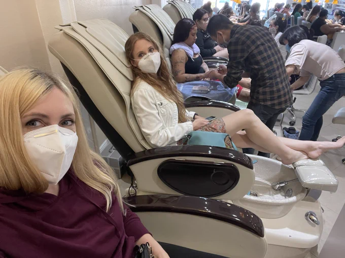 Selfie with my sister, wearing masks and sitting in pedicure chairs