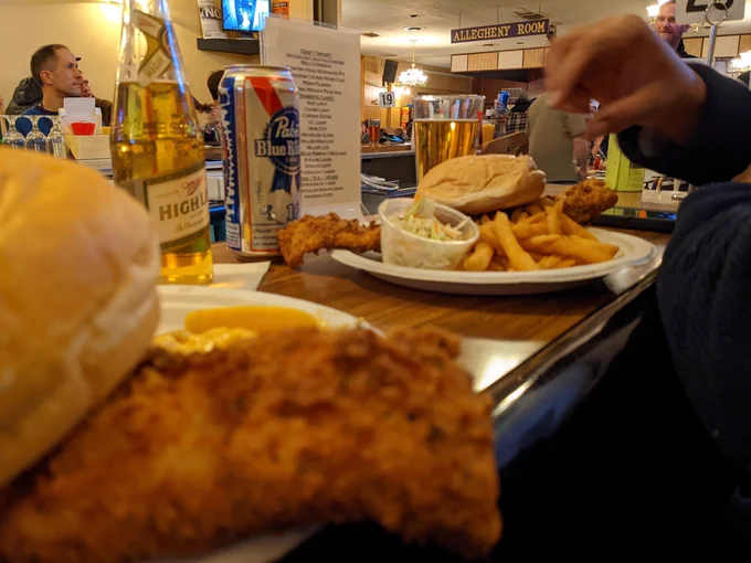 Plates with fried fish, french fries, and Cole slaw with a Miller High Life and Pabst Blue Ribbon on a bar