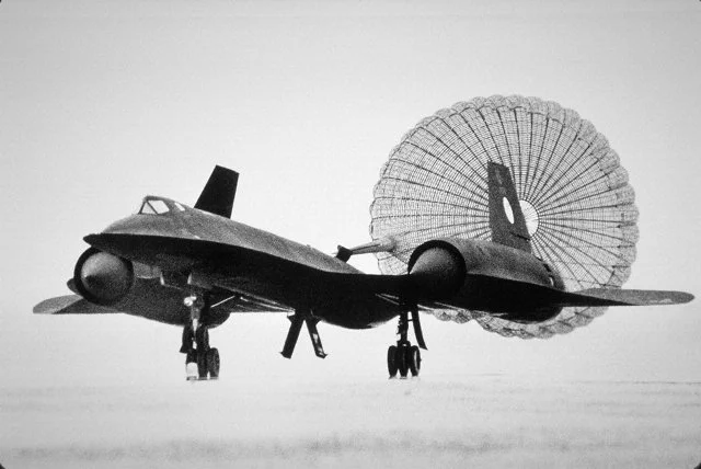 Black and white image of SR-71 Blackbird in flight with a parachute attached to its tail.