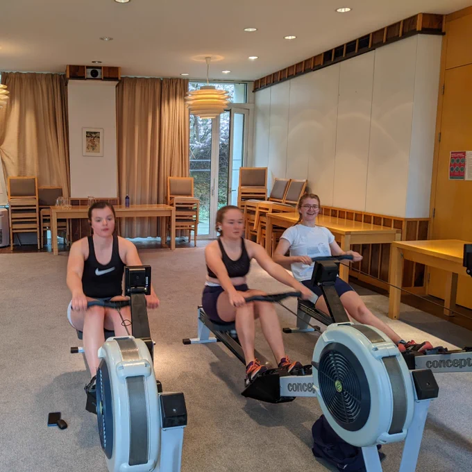 [Image Description]: Three rowers from the women's side using the ergs