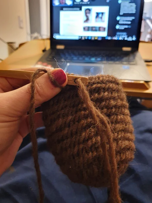 Brown wool toe section of a needlebound sock in front of a blurry laptop showing Microsoft Teams.