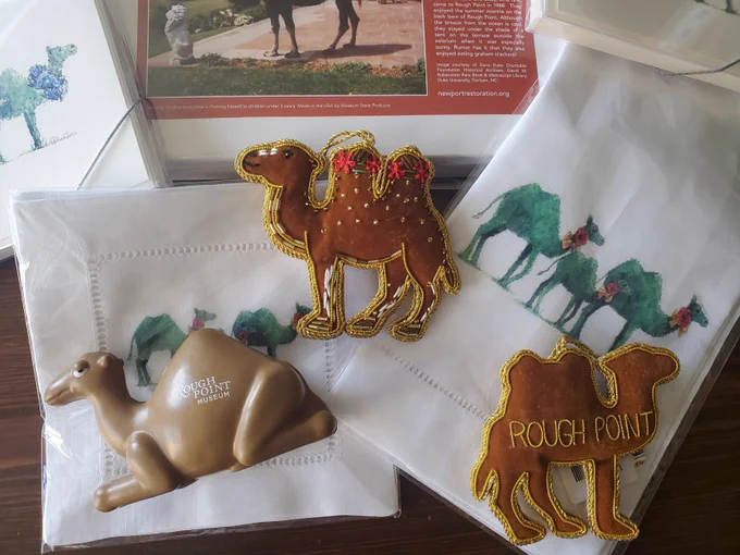 NRF Museum Store products featuring Bactrian camels, some with flowers and floral wreaths around their necks--including a puzzle, a fabric ornament with bead work, linen topiary camels, and a seated camel with the Rough Point Museum logo.