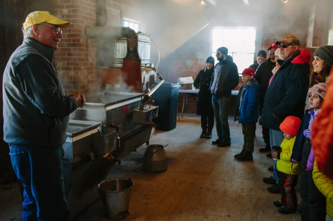 Brad Presby explains the sugaring process in front of two evaporators as an audience watches with steam above their heads.