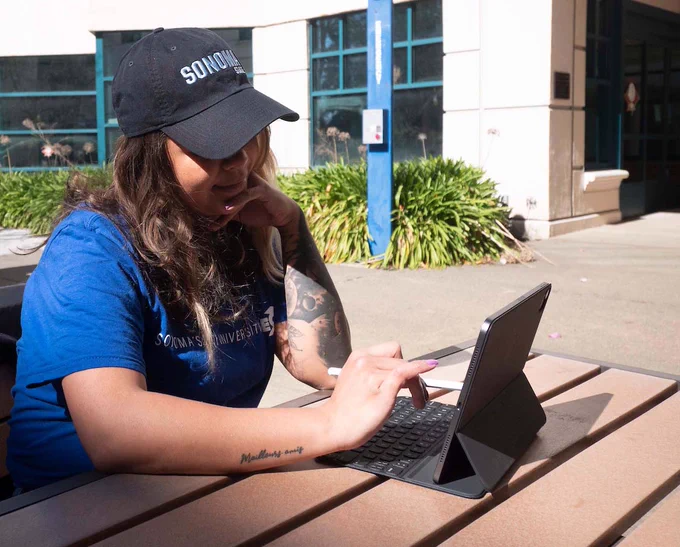 A college student sitting outdoors typing on a tablet computer.