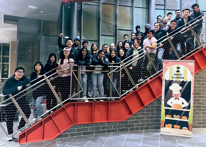  A large group of people stands on a staircase with red beams and smiles. 