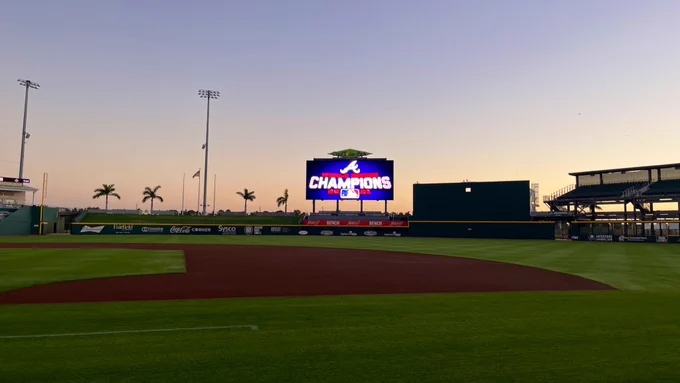 A picture from behind first base at cool today park as the sun rises in the sky beyond the outfield. On the centerfield Jumbotron is a 2021 Atlanta Braves World Series champions logo.