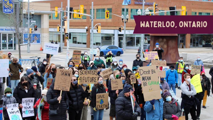 A group of activists stand in front of an RBC branch. They hold various signs that read "think or swim", "im voting for climate action", "scientists 4 future", "Indigenous sovereignty is climate justice", "save the earth", "the future in in our hands", and "strike for climate". Yellow text on a red label at the top right reads "Waterloo, Ontario"
