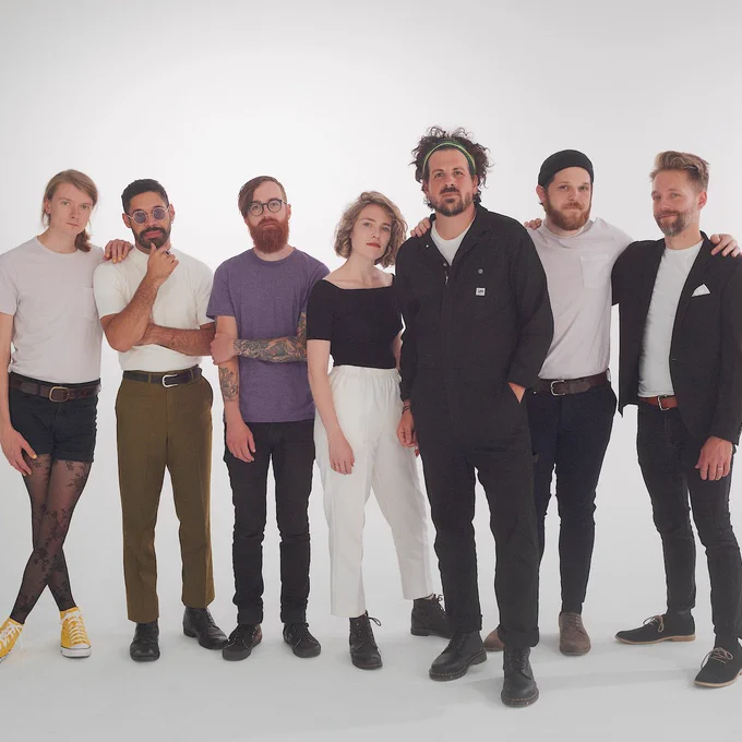 📷 of The Collection standing casually in front of a white backdrop.