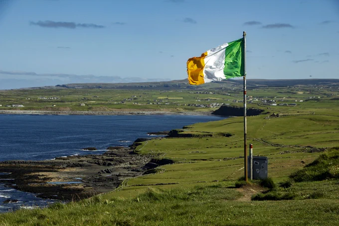 Irish flag flying on a flagpole at the edge of the the Cliffs of Moher, Clare, Ireland.