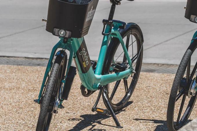 Teal electric bike with a black basket parked on a sidewalk