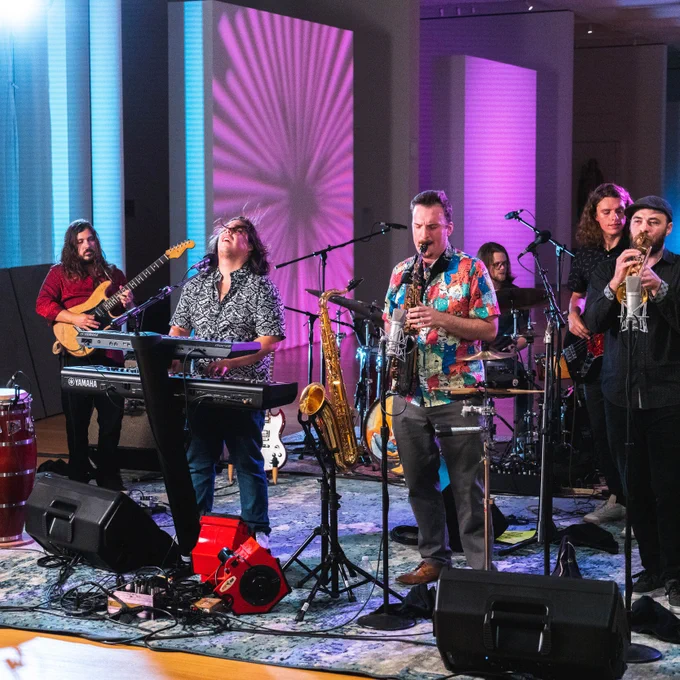 📷 of Tumbao playing a show with blue and purple screens in the background.