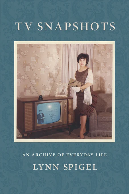 Cover of TV Snapshots: An Archive of Everyday Life by Lynn Spigel. Cover is of a blue wallpaper pattern, with a square picture at the center of a woman in 1962, dressed nicely and posed for a picture in her living room, next to a box tv set that is turned on to the news.