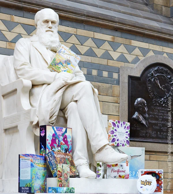 The statue of Charles Darwin in Hintze Hall holding a board game and with lots of board games by his feed.