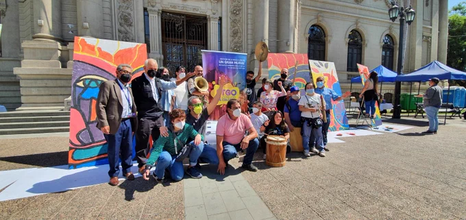 En el frontis del museo de Bellas Artes, un grupo de personas participantes de la actividad están reunidas delante de las obras pintadas, algunos levatan sus manos en señal de saludo. 