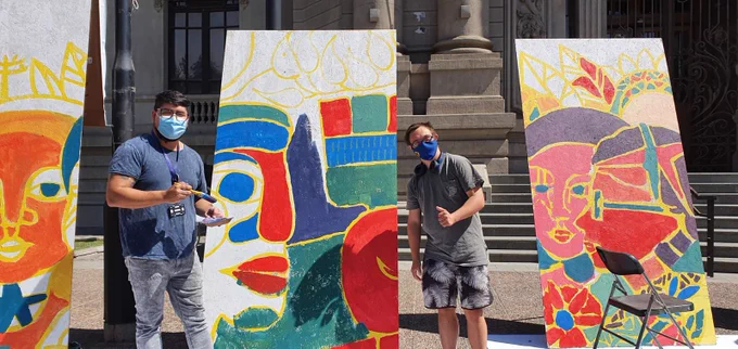 Joven con síndrome de Down y representante de una organización posan junto a dos lienzos que están pintando. 