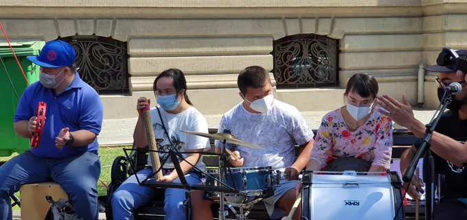 Cuatro jóvenes con síndrome de Down junto a sus instrumentos, pandero, palo de agua y batería, tocan una pieza musical durante la actividad, acompañados por su profesor. 