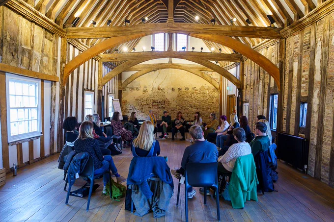 The group sit in a large circle under the arched beams of dragon hall, listening intently