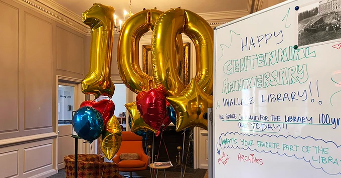 Gold balloon display reading 100 in celebration of Wallace Library's centennial. To the right of the balloon display is a white board reading happy centennial birthday Wallace Library! 