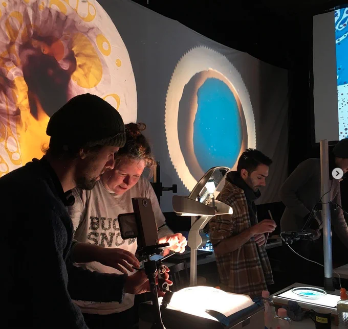 Liquid light show workshop participants working with overhead projectors, inks and dyes to create colourful reactions which are projected on the wall,
