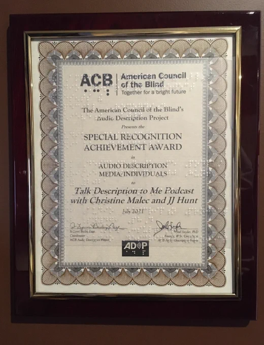 Special Recognition Award from the American Council of the Blind's Audio Description Project, presented to Christine Malec and JJ Hunt of the Talk Description to Me podcast, July 2021. Plaque framed in glossy red wood, with a Braille overlay on the glass.